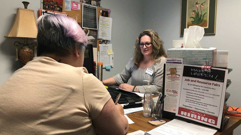 A lightly pink-haired female sits across the desk from a caseworker during an interview for financial assistance.