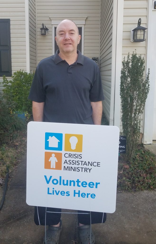Kurt poses outside his home with a Crisis Assistance Ministry Volunteer Lives Here sign.