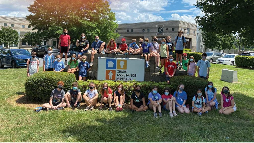 Group of youth pose in front of, beside, and on top of the Crisis Assistance Ministry sign outside their Charlotte, NC building