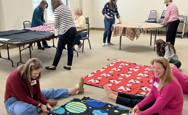 Smiling volunteers seated on the floor with colorful fleece fabric laid out to create no sew blankets.