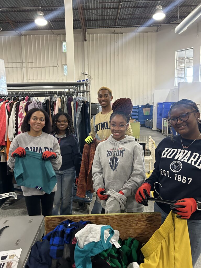 Group of Howard University students posing in the warehouse inspecting clothes.
