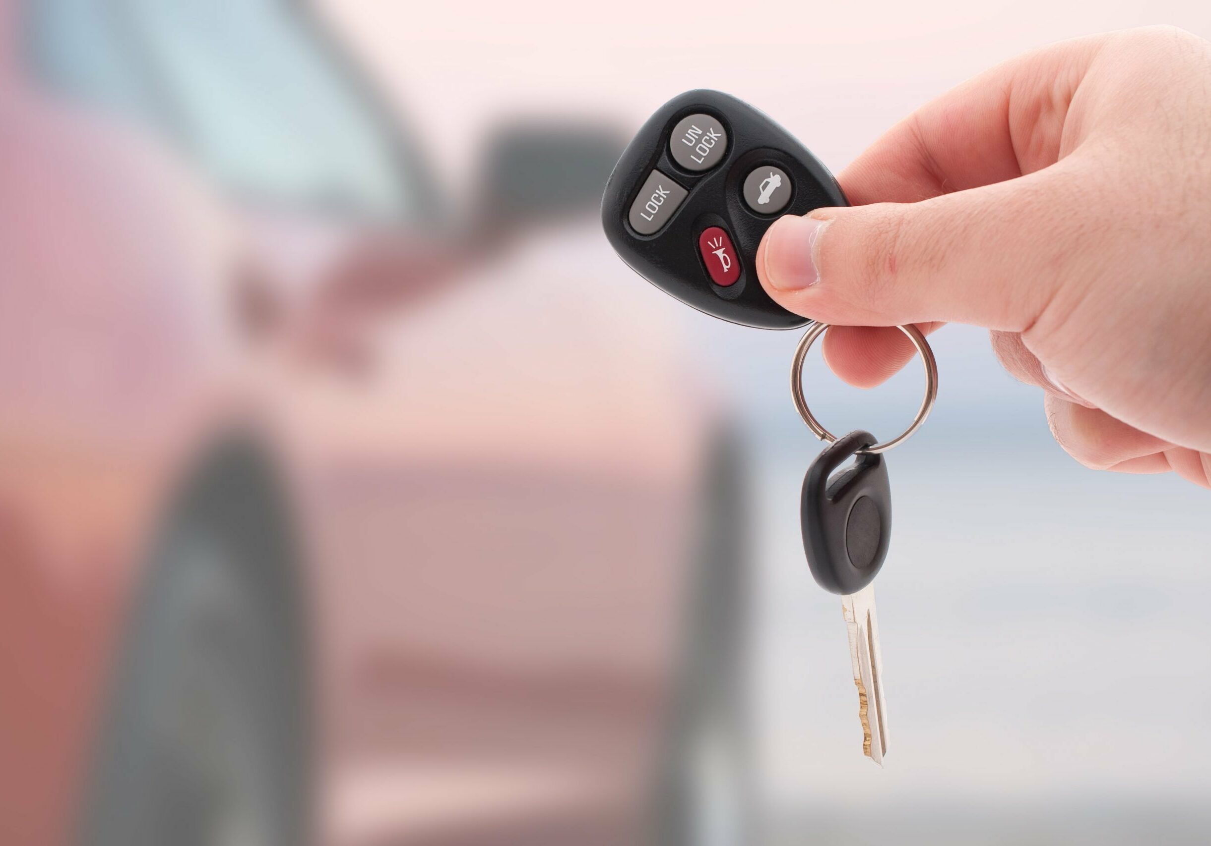 A hand holding car keys and a remote control for keyless entry.